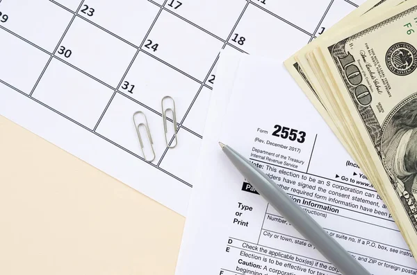 表格2553小企业公司的税务空白填写在日历页上，上面有笔和数百万美元的钞票 — 图库照片