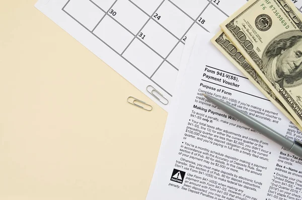 IRS Form 941-V Payment Voucher blank lies with pen and many hundred dollar bills on calendar page