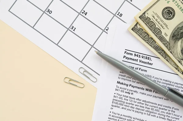 IRS Form 941-V Payment Voucher blank lies with pen and many hundred dollar bills on calendar page