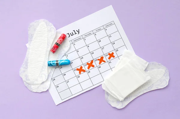 Menstrual pads and tampons on menstruation period calendar flat lay on lilac background — Stock Photo, Image