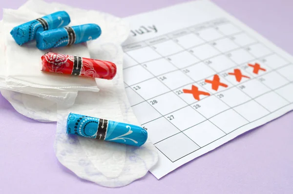 Cuscinetti mestruali e tamponi sul calendario del periodo mestruale con segni di croce rossa si trova su sfondo lilla — Foto Stock