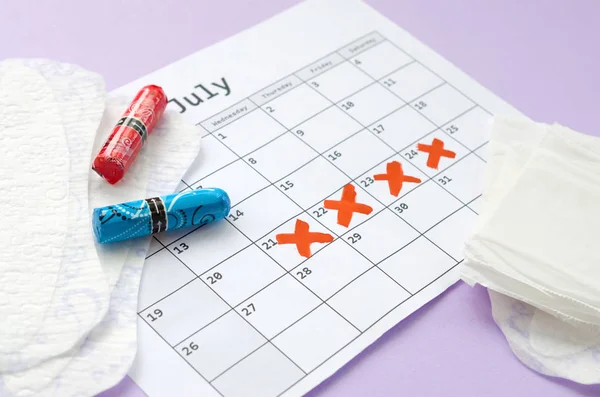 Cuscinetti mestruali e tamponi sul calendario del periodo mestruale con segni di croce rossa si trova su sfondo lilla — Foto Stock
