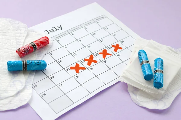 Menstrual pads and tampons on menstruation period calendar with red cross marks lies on lilac background — Stock Photo, Image