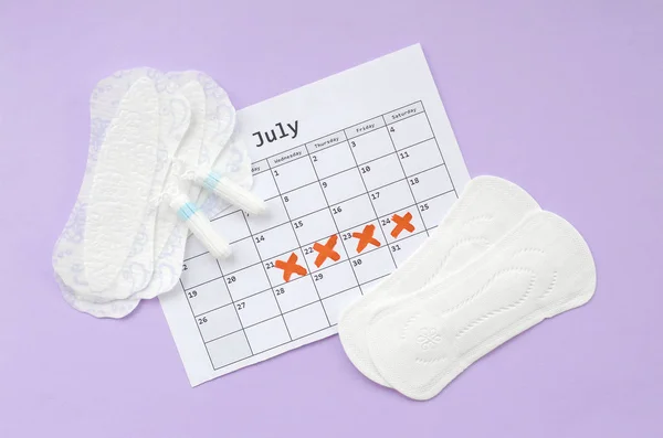 Menstruationspolster und Tampons auf Menstruationszeitkalender flach auf fliederfarbenem Hintergrund — Stockfoto