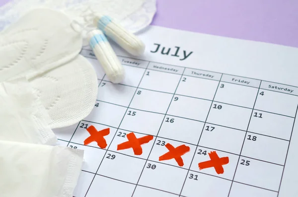 Menstruatie kussens en tampons op menstruatie periode kalender met rode kruismarkeringen ligt op lila achtergrond — Stockfoto