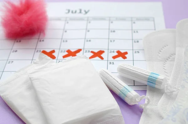 Cuscinetti mestruali e tamponi sul calendario del periodo mestruale con segni di croce rossa si trova su sfondo lilla — Foto Stock