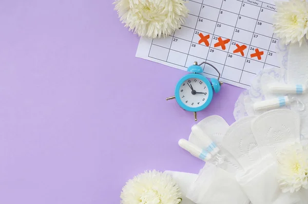 Cuscinetti mestruali e tamponi sul calendario del periodo mestruale con sveglia blu e fiori bianchi — Foto Stock