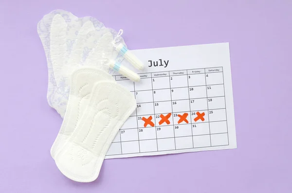 Menstruatie kussens en tampons op menstruatie periode kalender plat lag op lila achtergrond — Stockfoto