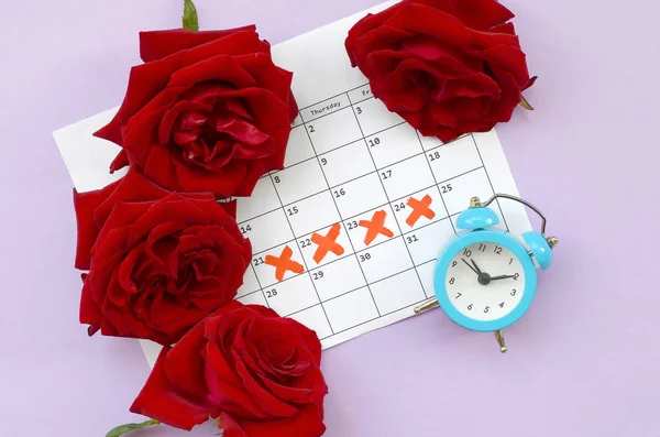 Reloj despertador azul y rosas rojas en el calendario del período menstrual con marcas de cruz roja — Foto de Stock