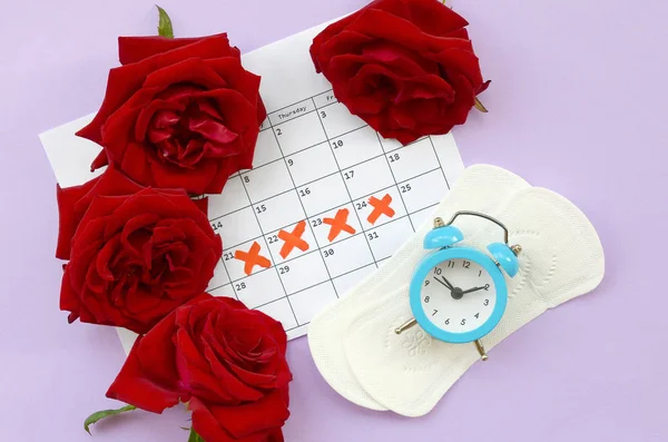 Menstrual pads on menstruation period calendar with blue alarm clock and red rose flowers