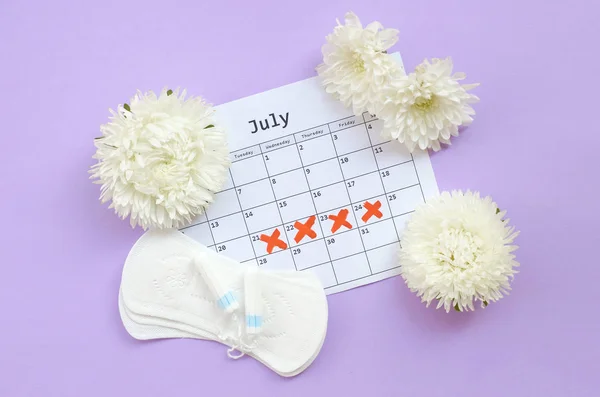 Almohadillas y tampones menstruales en el calendario del período de menstruación con flores blancas sobre fondo lila —  Fotos de Stock