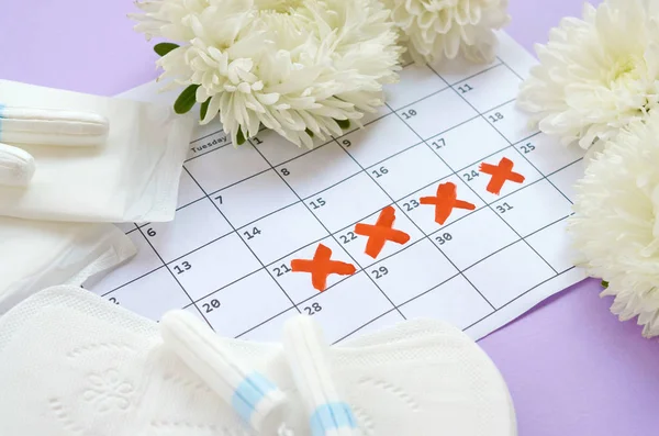 Cuscinetti mestruali e tamponi sul calendario del periodo mestruale con fiori bianchi su sfondo lilla — Foto Stock