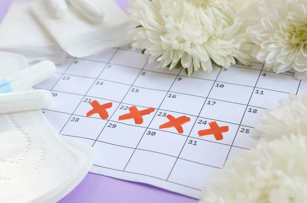 Cuscinetti mestruali e tamponi sul calendario del periodo mestruale con fiori bianchi su sfondo lilla — Foto Stock