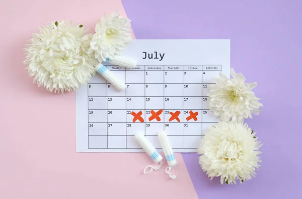 Tampones menstruales en el calendario del período de menstruación con flores blancas sobre fondo lila y rosa — Foto de Stock