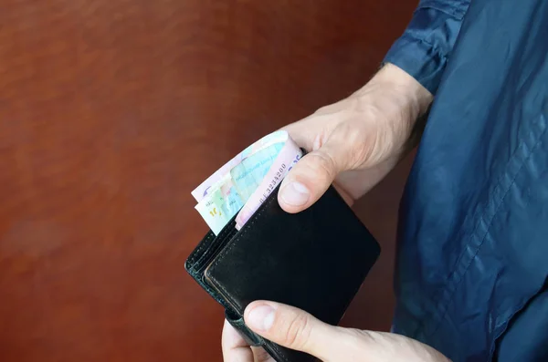 Людина тримає в руках чорний шкіряний гаманець з україніанськими грошима або злодієм, який вкрав гаманець з грошима. — стокове фото