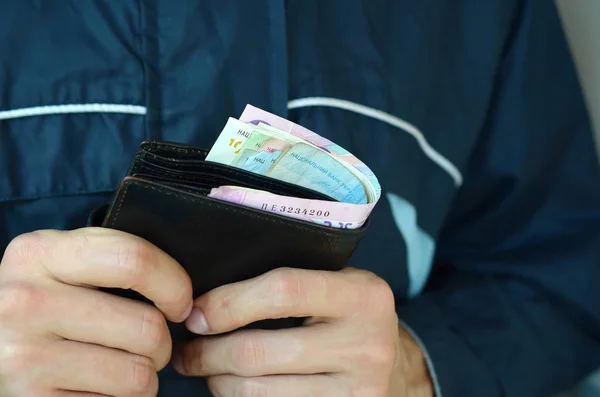 Mężczyzna trzyma w rękach czarny skórzany portfel z ukraińskich pieniędzy lub złodzieja, który ukradł portfel pełen pieniędzy — Zdjęcie stockowe