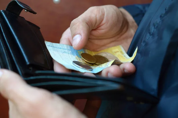 Mani maschili con monete con piccole banconote ucraine e vecchia borsa nera — Foto Stock