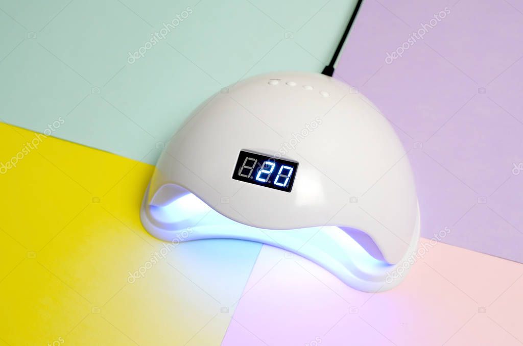 UV LED nail lamp for curing process by gel method lies on pastel multi colored table