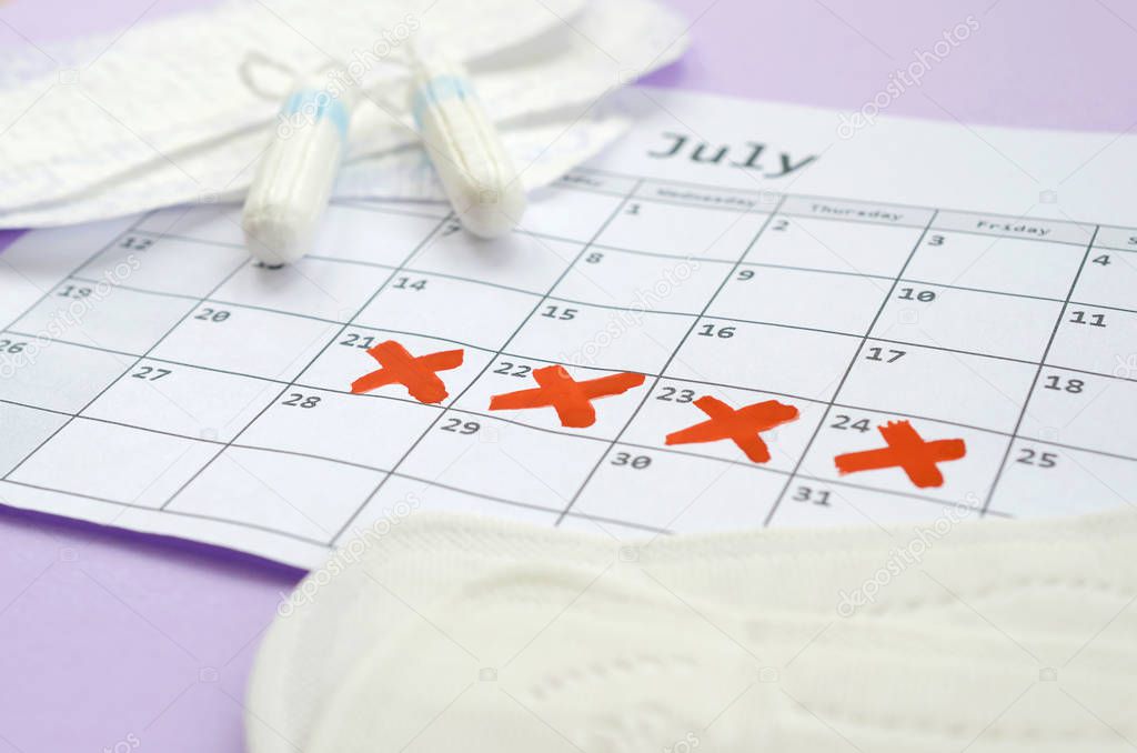 Menstrual pads and tampons on menstruation period calendar with red cross marks lies on lilac background