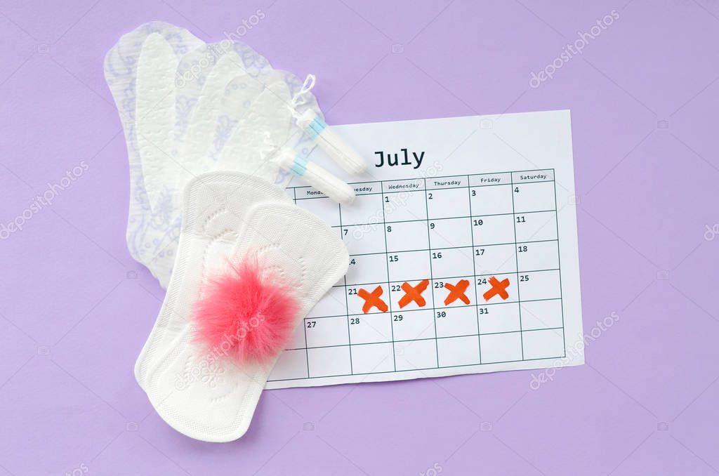 Menstrual pads and tampons on menstruation period calendar flat lay on lilac background