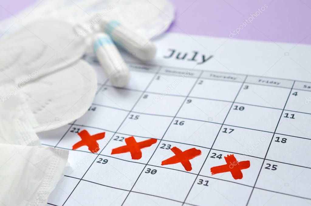 Menstrual pads and tampons on menstruation period calendar with red cross marks lies on lilac background