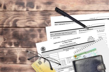 USCIS form I-485 Application to register permanent residence or adjust status lies on flat lay office table and ready to fill. U.S. Citizenship and Immigration services paperwork concept. Top view clipart