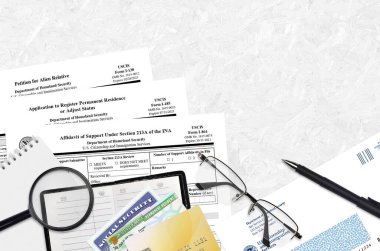 I-130 Uzaylı akraba dilekçesi, I-485 Daimi ikamet kaydı ya da statü ayarlama başvurusu ve I-864 maddesinin 213A maddesi altında destek beyannamesi masada ve doldurulmaya hazır.