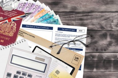 HM gelir ve gümrük sertifikası ile İngiliz Vergi formu P60 yıl sonu sertifikası ofis eşyalarıyla birlikte masadadır. İngiltere Birleşik Krallığında HMRC evrakları ve vergi ödeme süreci