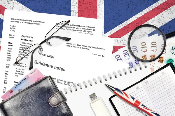 English form BRP with guidance notes to applying biometric residence permit card from UK visas and immigration services lies on table with office items. UK residence permit paperwork process