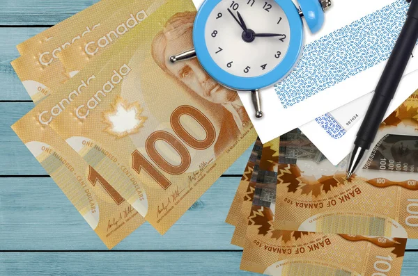 100 Canadian dollars bills and alarm clock with pen and envelopes. Tax season concept, payment deadline for credit or loan. Financial operations using postal service. Quick money transfer