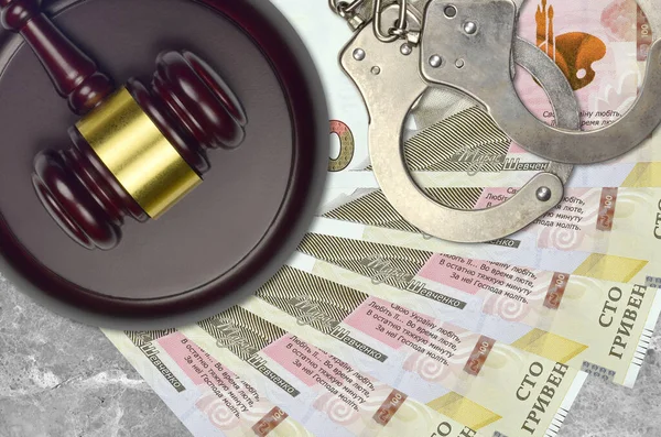 100 Ukrainian hryvnias bills and judge hammer with police handcuffs on court desk. Concept of judicial trial or bribery. Tax avoidance or tax evasion
