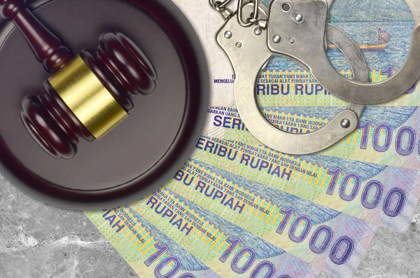 1000 Indonesian rupiah bills and judge hammer with police handcuffs on court desk. Concept of judicial trial or bribery. Tax avoidance or tax evasion