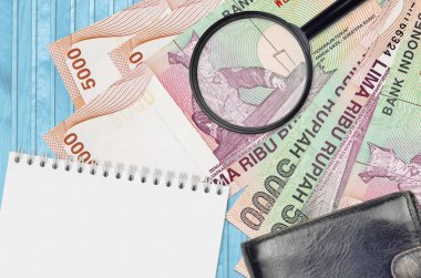 5000 Endonezya rupiası ve siyah çantalı ve not defterli büyüteç. Sahte para konsepti. Sahte parayı tespit etmek için para banknotlarındaki farklılıkları araştır