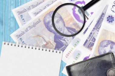 20 British pounds bills and magnifying glass with black purse and notepad. Concept of counterfeit money. Search for differences in details on money bills to detect fake money clipart