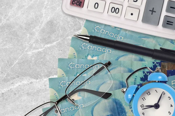 5 Canadian dollars bills and calculator with glasses and pen. Business loan or tax payment season concept. Financial planning and time to pay taxes