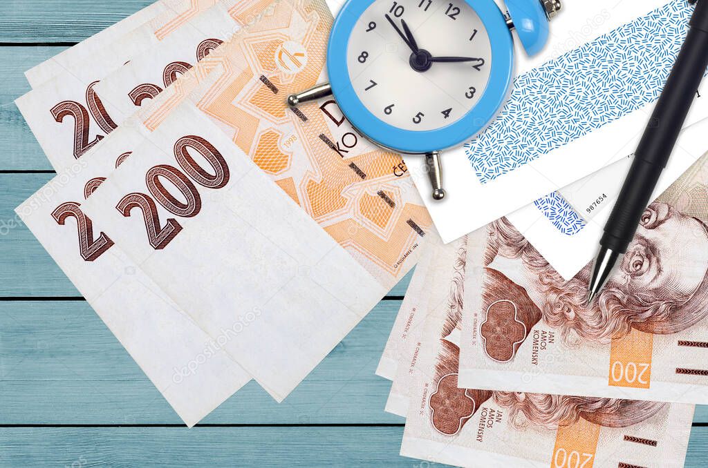 200 Czech korun bills and alarm clock with pen and envelopes. Tax season concept, payment deadline for credit or loan. Financial operations using postal service. Quick money transfer