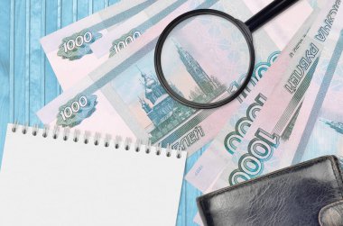 1000 Rus rublesi ve siyah çantalı ve not defterli büyüteç. Sahte para konsepti. Sahte parayı tespit etmek için para banknotlarındaki farklılıkları araştır