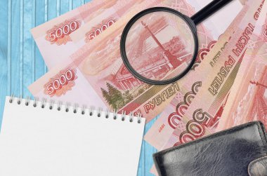 5000 Rus rublesi ve siyah çantalı ve not defterli büyüteç. Sahte para konsepti. Sahte parayı tespit etmek için para banknotlarındaki farklılıkları araştır