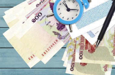 100 Kamboçyalı isyan faturası ve içinde kalem ve zarflar olan çalar saat. Vergi sezonu konsepti, kredi veya kredi için ödeme tarihi. Posta servisini kullanarak finansal operasyonlar. Hızlı para transferi