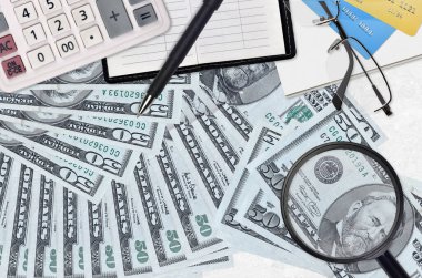 50 dolarlık banknotlar, hesap makinesi, gözlük ve kalem. Vergi ödeme sezonu kavramı veya yatırım çözümleri. Yüksek maaşlı bir iş arıyorum.