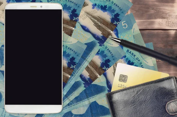 5 Canadian dollars bills and smartphone with purse and credit card. E-payments or e-commerce concept. Online shopping and business with portable devices usage