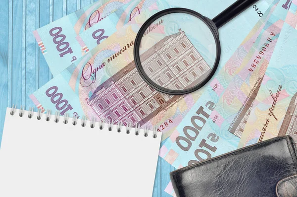 1000 Ukrainian hryvnias bills and magnifying glass with black purse and notepad. Concept of counterfeit money. Search for differences in details on money bills to detect fake money