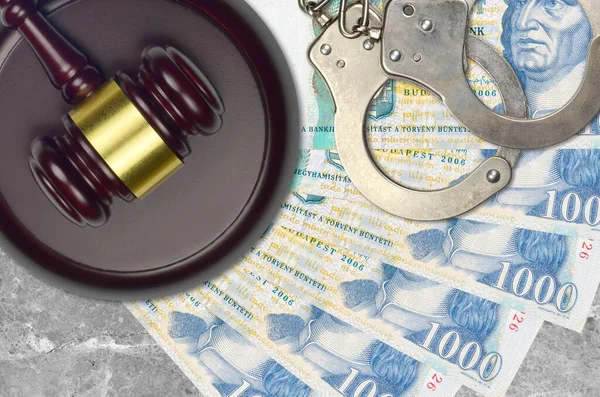 1000 Hungarian forint bills and judge hammer with police handcuffs on court desk. Concept of judicial trial or bribery. Tax avoidance or tax evasion