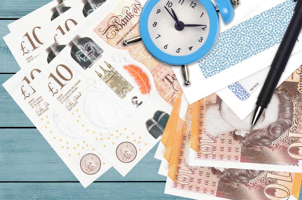 10 British pounds bills and alarm clock with pen and envelopes. Tax season concept, payment deadline for credit or loan. Financial operations using postal service. Quick money transfer