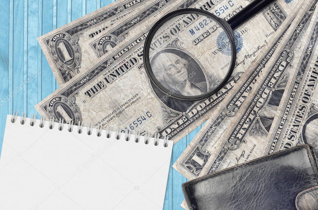 1 US dollar bills and magnifying glass with black purse and notepad. Concept of counterfeit money. Search for differences in details on money bills to detect fake money