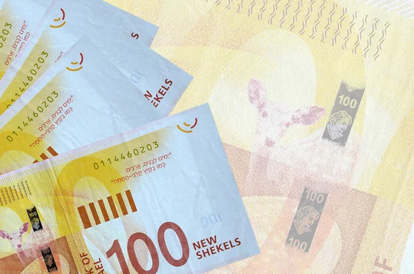 100 Israeli new shekels bills lies in stack on background of big semi-transparent banknote. Abstract business background with copy space