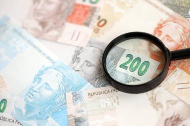 Brezilya reais banknotları ve büyüteç. Mevcut Brezilya gerçek para faturaları ve loupe büyük miktarda masada yatıyor. Brezilya 'da mali izleme ve vergilendirme kavramı