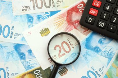 Israel New Shekels banknotları ve büyüteçle birlikte hesap makinesi. Mevcut İsrail para faturaları ve loupe ile calc büyük miktarda masada yatıyor. İsrail 'de vergilendirme ve para kavramı