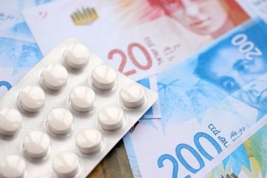 Israel New Shekels banknotları ve ilaç hapları. Mevcut İsrail para ve uyuşturucu faturaları büyük miktarda masada yatıyor. İsrail 'de ilaç ve eczane kavramı