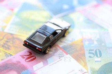 İsviçre frangı banknotları ve oyuncak araba. Mevcut frank, faturalar ve siyah araba büyük miktarda masada yatıyor. İsviçre 'de araba sahibi olma kavramı